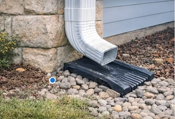 White downspout draining onto a splash block over river rock