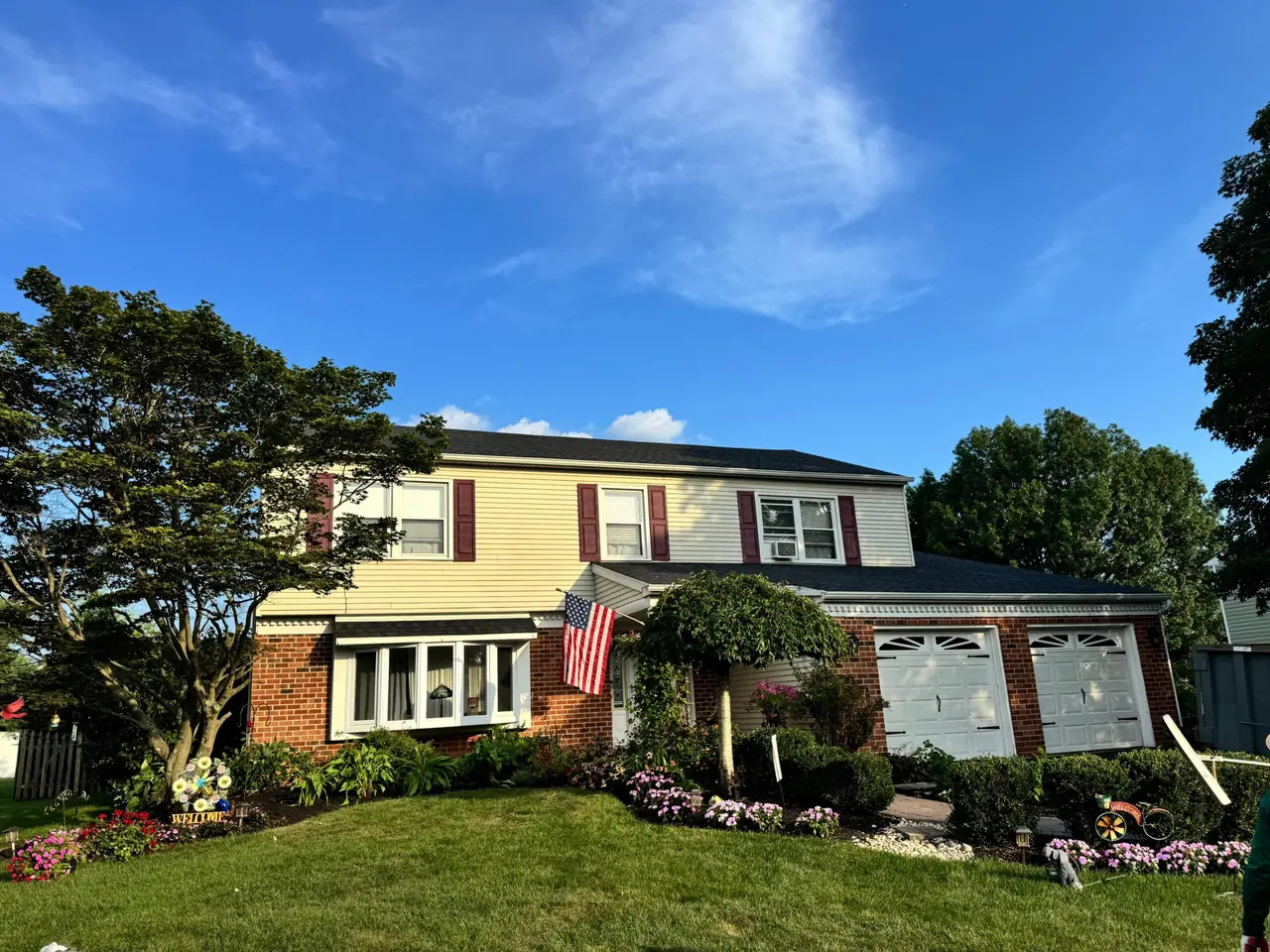 Two-story brick and siding colonial with an American flag and a dark shingle roof