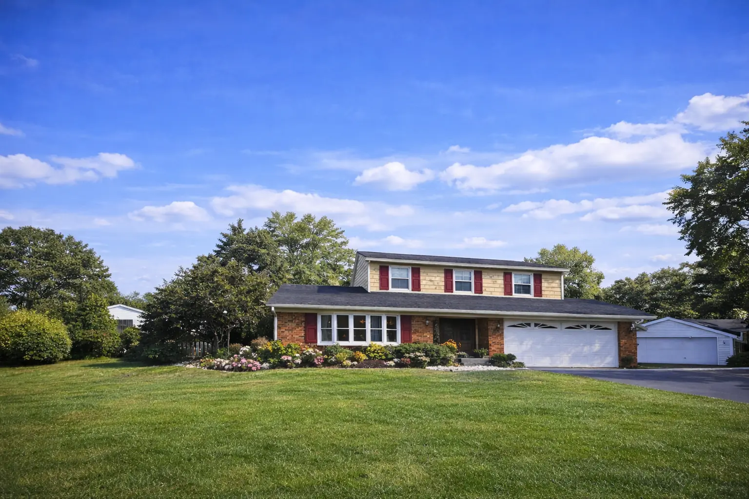 Two-story brick and cedar-sided home with red shutters and a dark shingle roof on a wide lawn