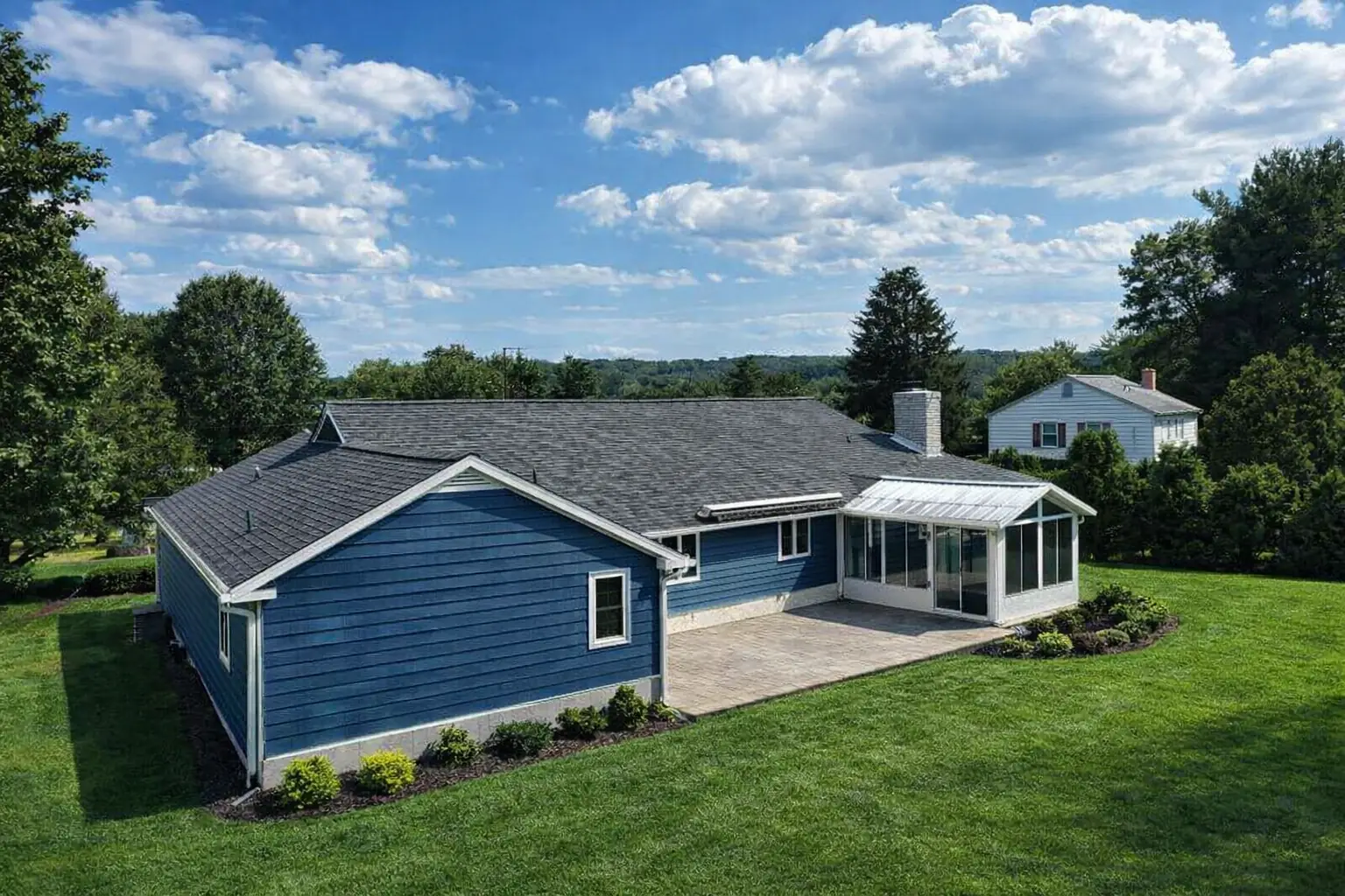 Blue ranch home with a new gray shingle roof and a sunroom on a wide lawn