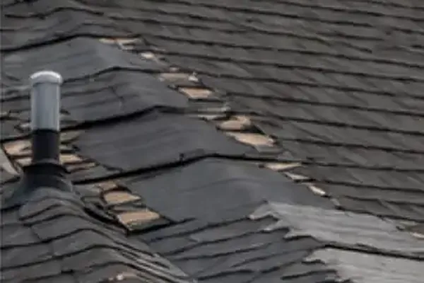Wind damaged roof with lifted and torn shingles